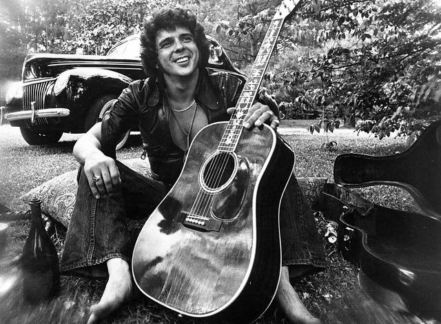 1975: Songwriter and guitarist Bobby Whitlock poses for a portrait in front of an old car next to a bottle of Dom Perignon champagne holding an acoustic guitar in circa 1975. (Photo by Michael Ochs Archives/Getty Images)